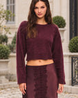 LoveShackFancy Bellaman Pullover in merlot, on model in a townhouse courtyard